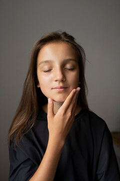 Girl With Eyes Closed Touching Face Against Gray Wall