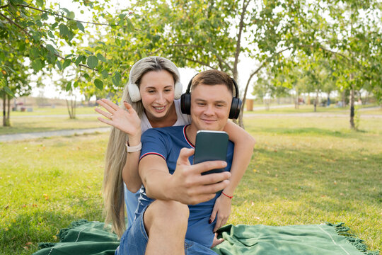 Young Man On Video Call Through Smart Phone With Girlfriend Waving From Behind