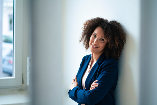 Smiling businesswoman with curly hair leaning on wall