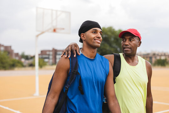Mature man talking with son walking at basketball court