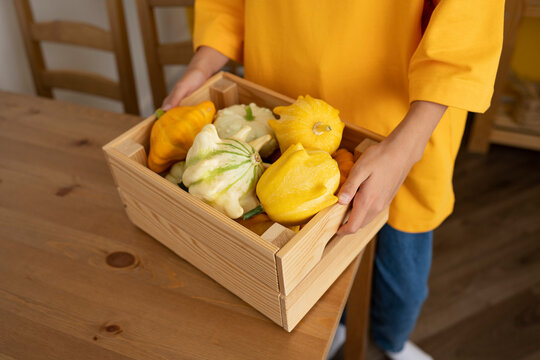 Girl holding crate of pumpkins at table