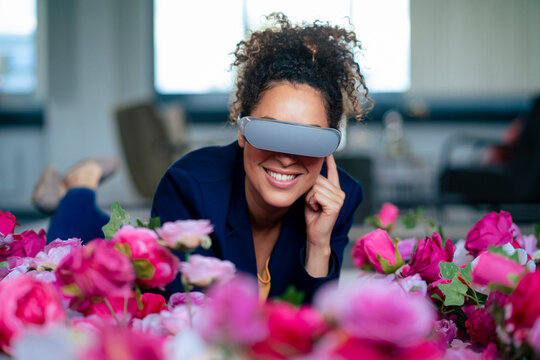 Smiling businesswoman using VR glasses by flowers at office