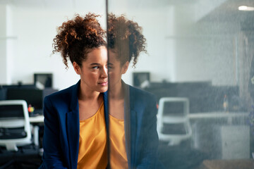 Thoughtful businesswoman with reflection on glass wall in office