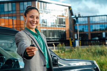 Businesswoman with key and car in front of office building on sunny day