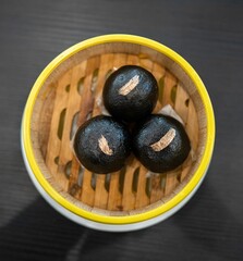 Closeup of black steamed dim sum in a bamboo steamer