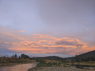 Beautiful cloudy sky at sunset over the river. The high bank of the river is overgrown with grass.