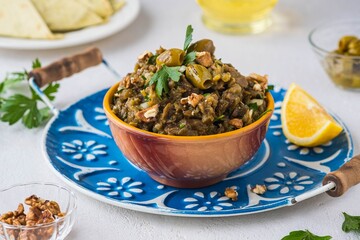 Appetizer, salad of baked eggplant, onions, herbs and spices in a ceramic bowl on a blue tray on a light concrete background. eggplant recipes.