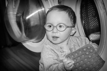 A little boy with glasses plays with a washing machine.