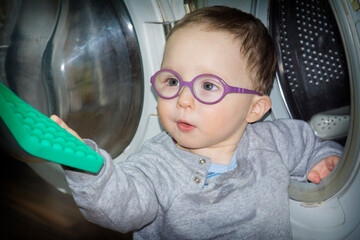 A little boy with glasses plays with a washing machine.