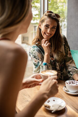 Stylish young women having friendly meeting with cups of coffee while sitting at table and chatting