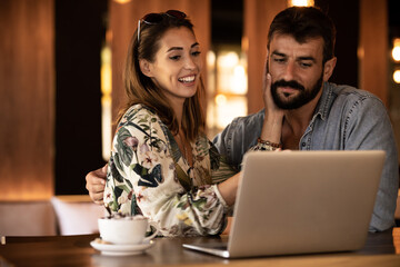 Happy couple using laptop at cafe enjoying time together