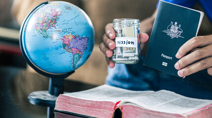Hand holding passport and savings jars full of money for mission, christian concept.