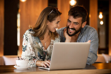 Happy couple using laptop at cafe enjoying time together