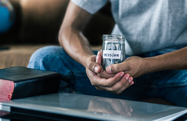 Savings jars full of money for mission in hands of christian male, christian concept.