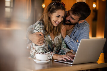 Happy couple using laptop at cafe enjoying time together
Smiling looking at each other
