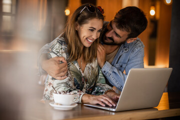Happy couple using laptop at cafe enjoying time together
Smiling looking at each other
