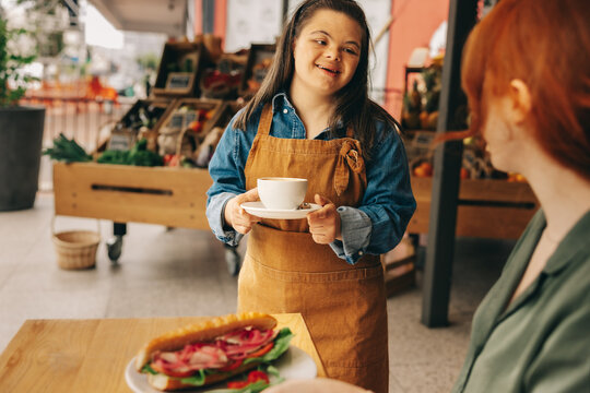 Friendly waitress with Down syndrome serving a customer in a cafe