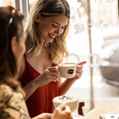 Beautiful happy women talking and laughing while drinking coffee together in coffee shop.
