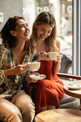 Beautiful happy women talking and laughing while drinking coffee together in coffee shop.