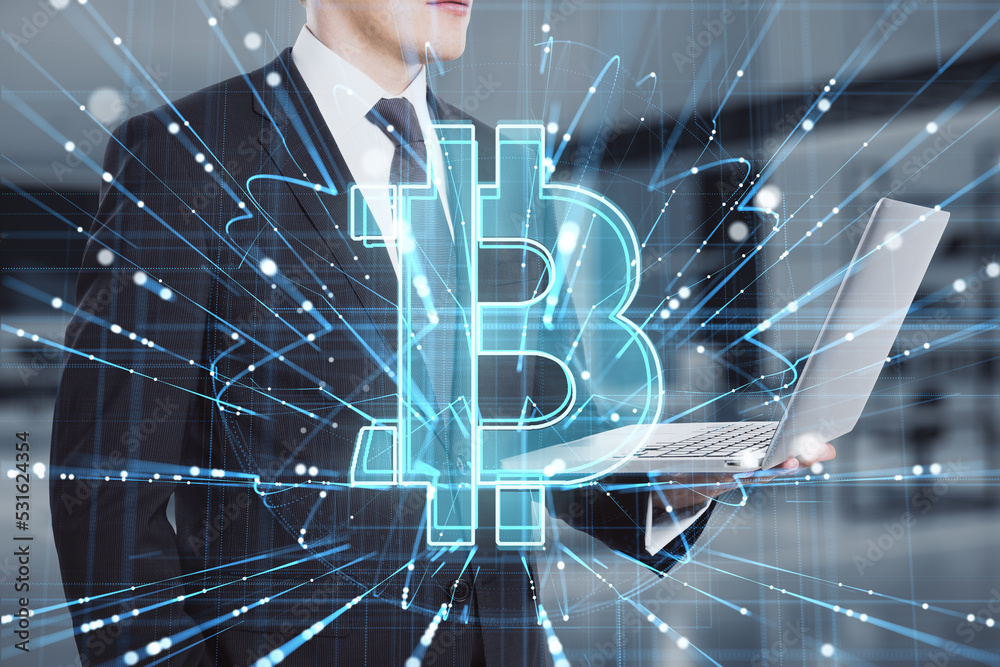 Poster close up of businessman hand using laptop with abstract glowing holographic bitcoin icon on blurry o