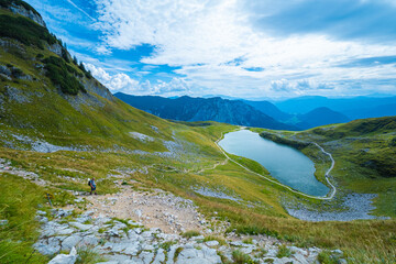 View of a single hiker, hiking on the stony path at Loser Mountain, Altaussee, Austria, with the Augstsee and the Atterkogel peak in the background