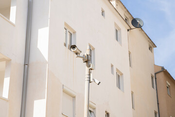 Fototapeta na wymiar two white surveillance cameras hang on a pole against the background of high-rise buildings in the big city. Security cameras.