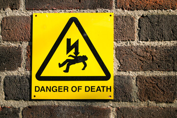 A bright yellow sign that says danger of death with an image of a lighting bolt hitting someone in...