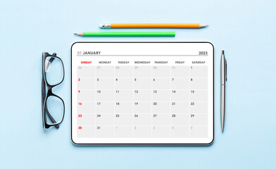 Tablet with calendar app, eyeglasses and office supplies