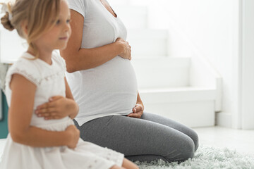 Pregnant mother and little daughter sitting on floor and practicing yoga