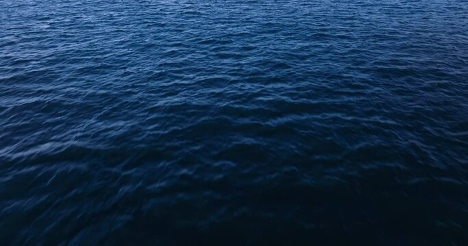 Low horizon aerial view flying over blue ocean water texture 