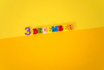 December 3 on a yellow and paper background with wooden and multicolored letters with space for text.