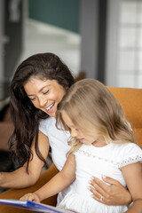 Obraz na płótnie Canvas Young mother and her cute little daughter,mom is reading a book to her. Family time concept