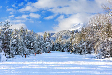 Bansko, Bulgaria perspective of groomed ski run slope, forest and mountain peaks panorama