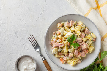 Russian Christmas or New Year salad Olivier from boiled vegetables and sausage with mayo on white table with fork