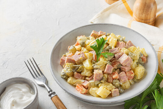 Traditional Russian or Ukrainian salad Olivier from boiled vegetables and sausage with mayo on white table with fork