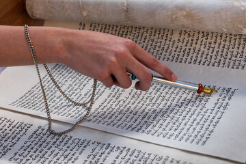 Closeup of a hand holding a yad or pointer to guide the reader through the Hebrew text of the Jewish Torah.