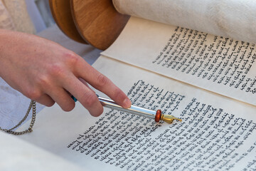 Closeup of a hand holding a yad or pointer to guide the reader through the Hebrew text of the Jewish Torah.