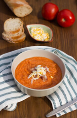 Cold Italian salmorejo soup with grated egg in a bowl on a striped napkin on a table.