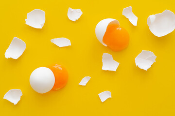 Top view of natural yolks and cracked egg shells on yellow background.