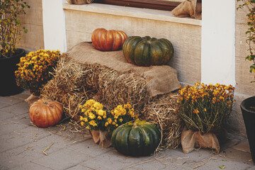 Pumpkins with flowers and rustic hay decoration outdoors. Stylish autumn decor of exterior building
