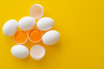 Top view of eggs and yolks in shells on yellow background.