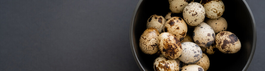 Top view of natural quail eggs in bowl on black surface, banner.