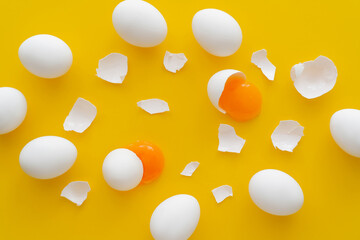 Top view of eggs near yolks and cracked shells on yellow background.