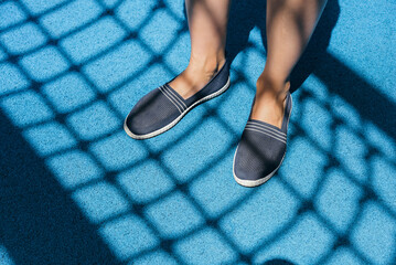 Slip-ons of dark blue color on female legs. Bright blue rubber running track.