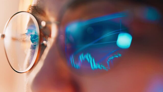 Closeup - Female eyes in eyeglasses late at night scrolling in front of laptop. Coder, she checking Bitcoin price chart on digital exchange on computer, cryptocurrency future price action prediction