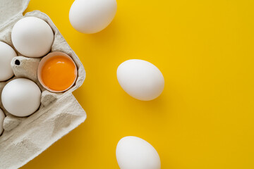 Top view of eggs near fresh yolk in shell in container on yellow background.