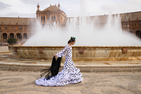Female flamenco dancer, teenage brunette and beautiful typical Spanish dancer is dancing with a black shawl in front of a fountain in a square in seville. Flamenco concept of world cultural heritage.