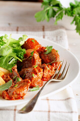 Close up of beef stew with herbs, chips and salad in dish on white wooden background.
