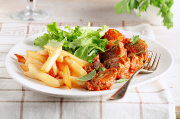 Close up of beef stew with herbs, chips and salad in dish on white wooden background.