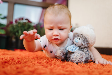 Baby lying on tummy with toy bear on floor. Portrait of baby a crawling on terrace. Adorable baby boy in patio. Newborn child playing.